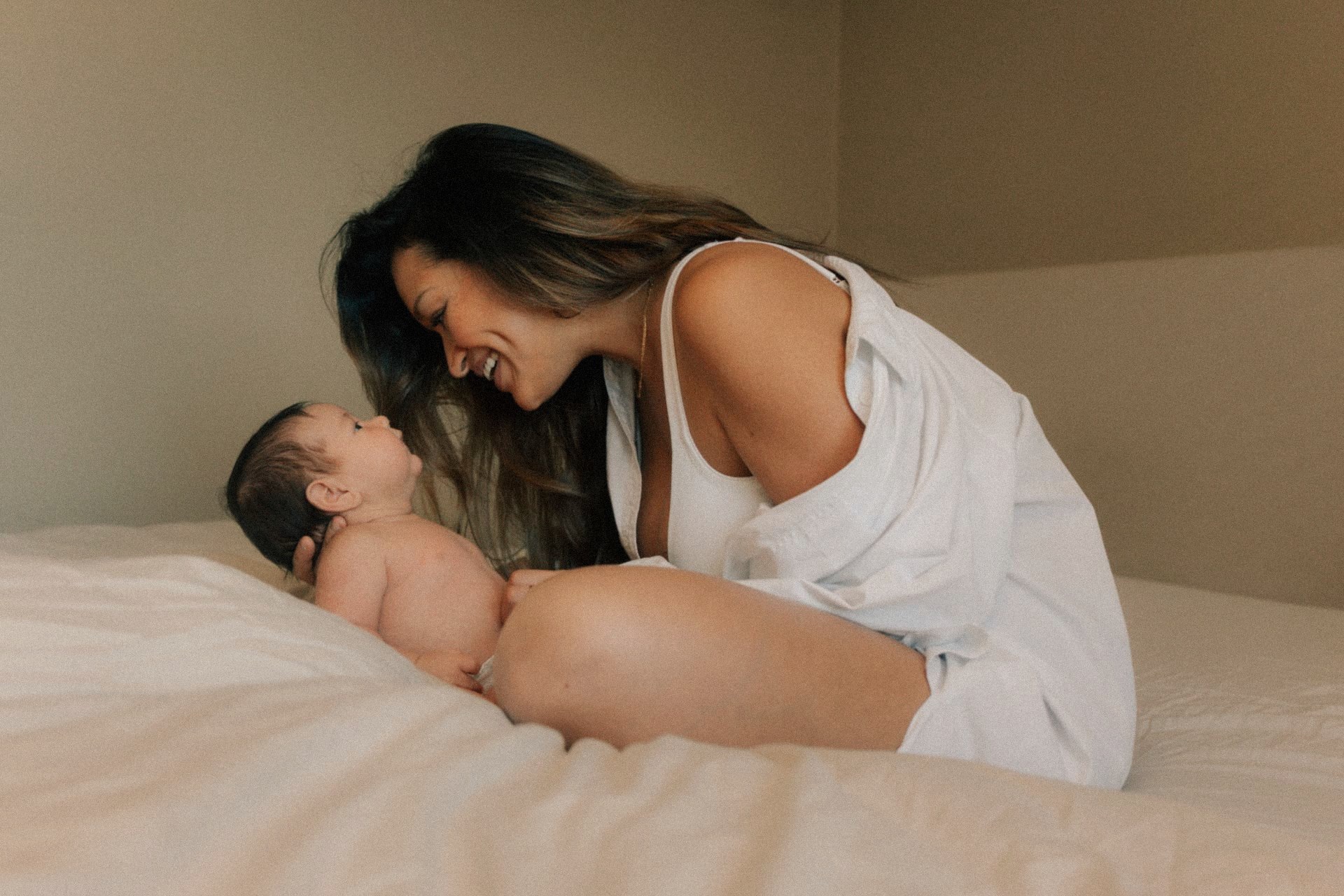 Moeder lacht neus aan neus met haar newborn op bed