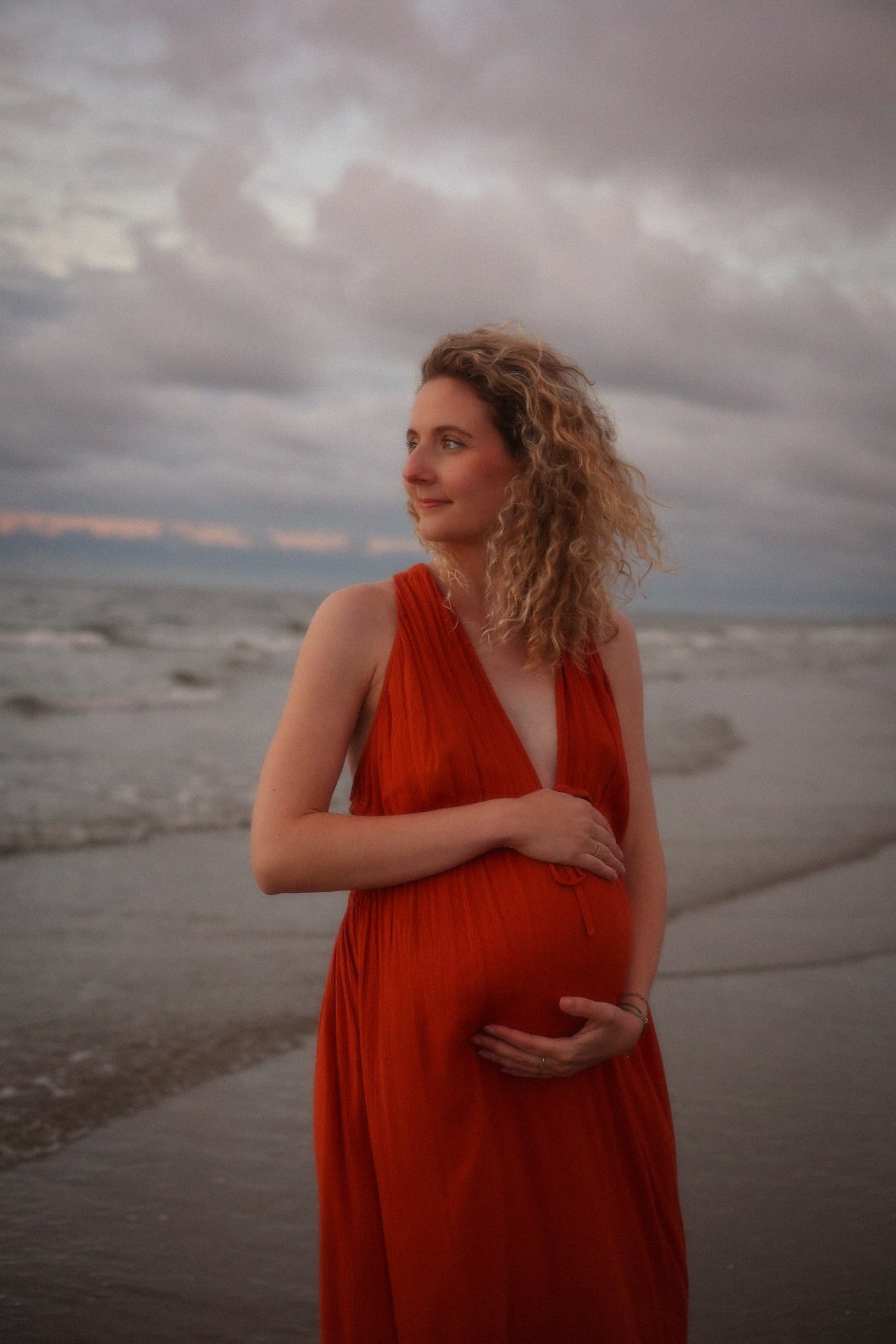 Zwanger portret in rode jurk aan zee