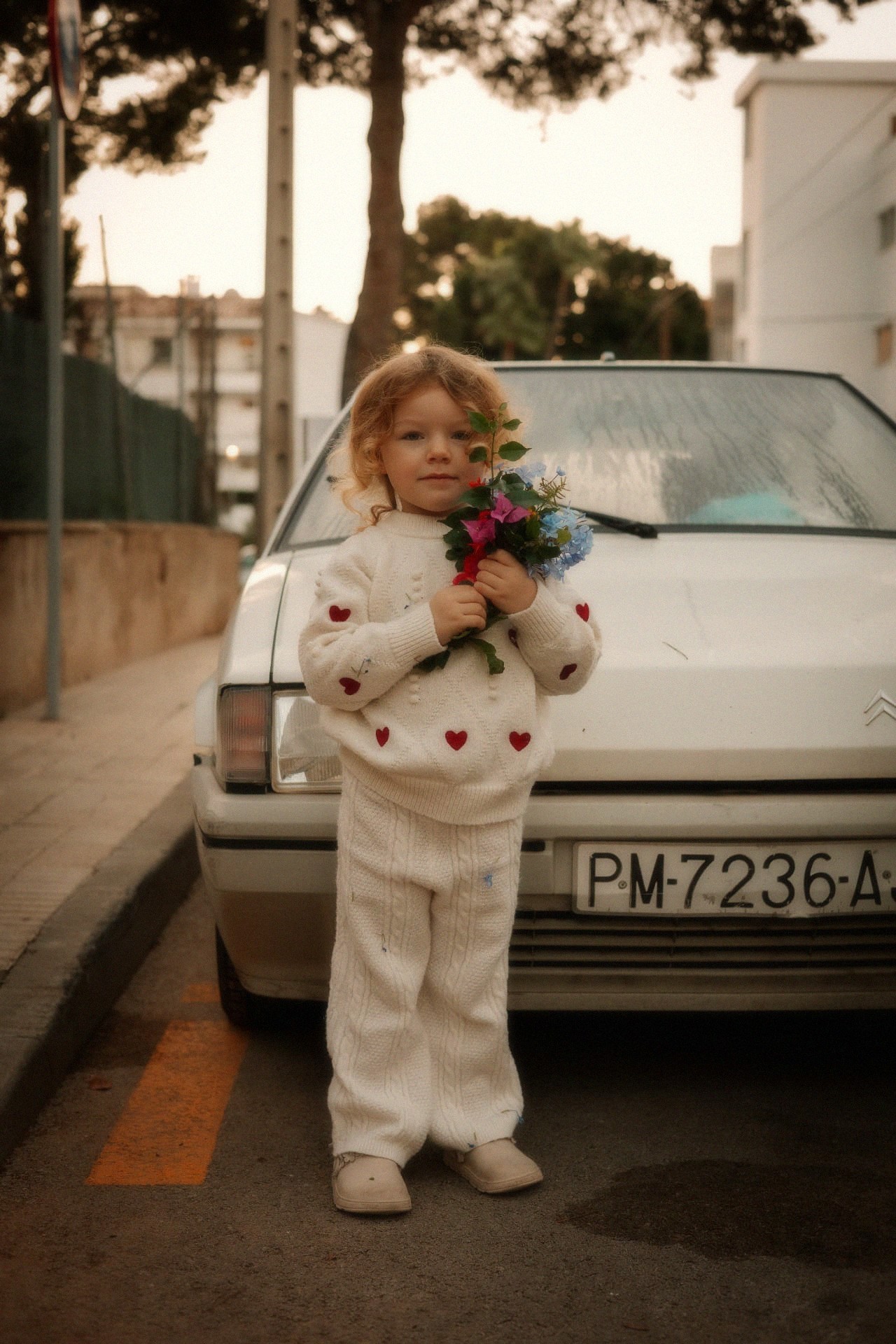 Meisje met boeket bloemen staat voor een oude auto in avondlicht