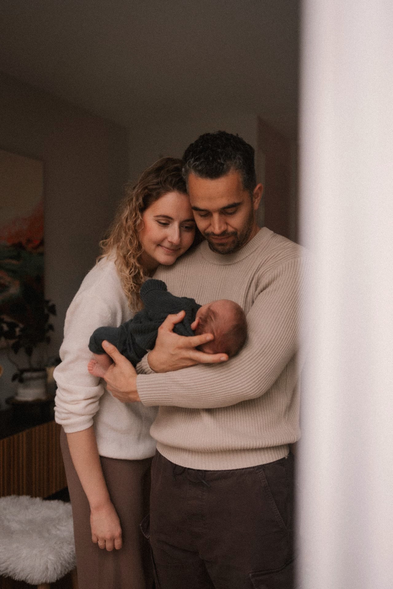 Ouders knuffelen samen hun newborn in zacht thuislicht