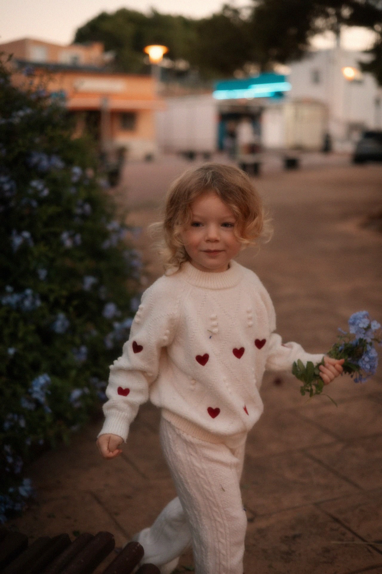 Meisje loopt lachend over een pleintje met bloemen in haar hand