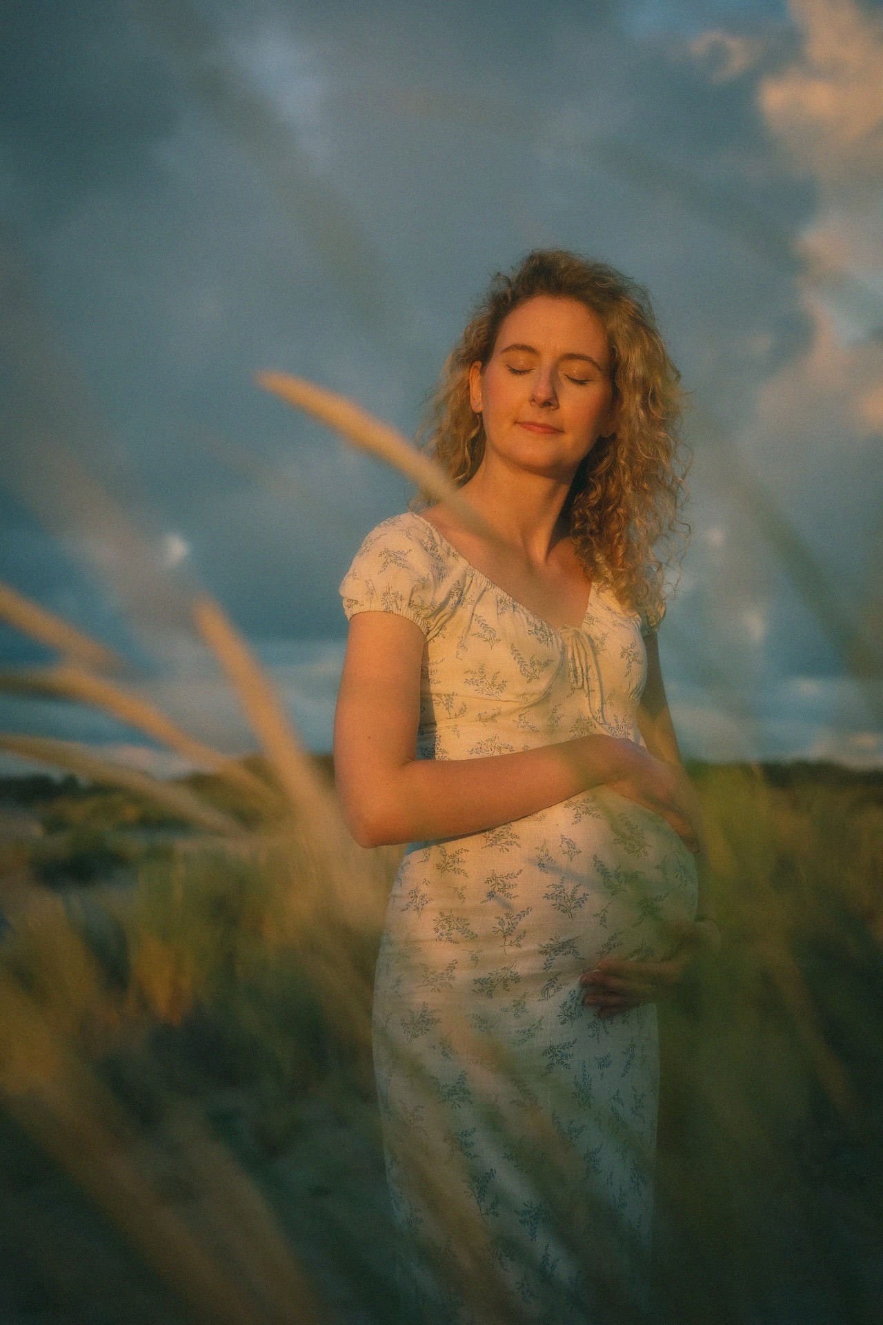 Zwanger portret met gesloten ogen tussen het helmgras in gouden avondlicht