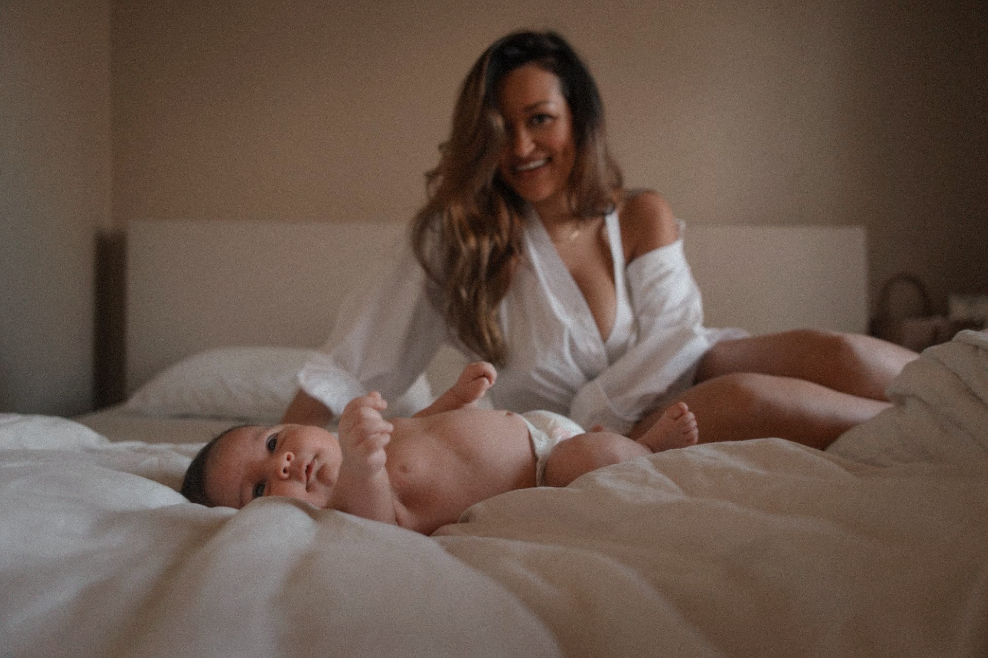 Newborn ligt lachend op bed terwijl mama toekijkt