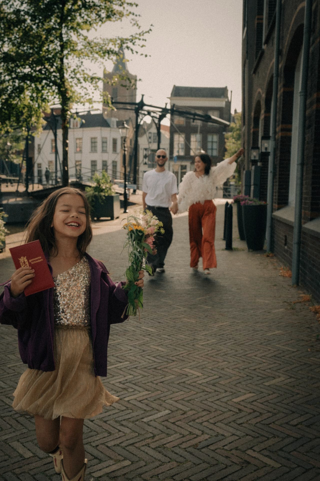 Dochter rent lachend voorop met het trouwboekje, ouders volgen hand in hand