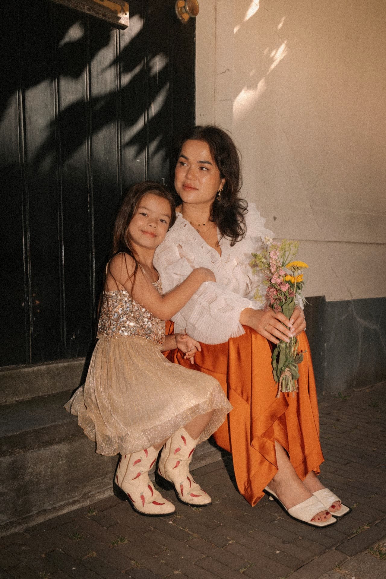Moeder en dochter in feestjurken zitten samen op een stoepje met een plukboeket